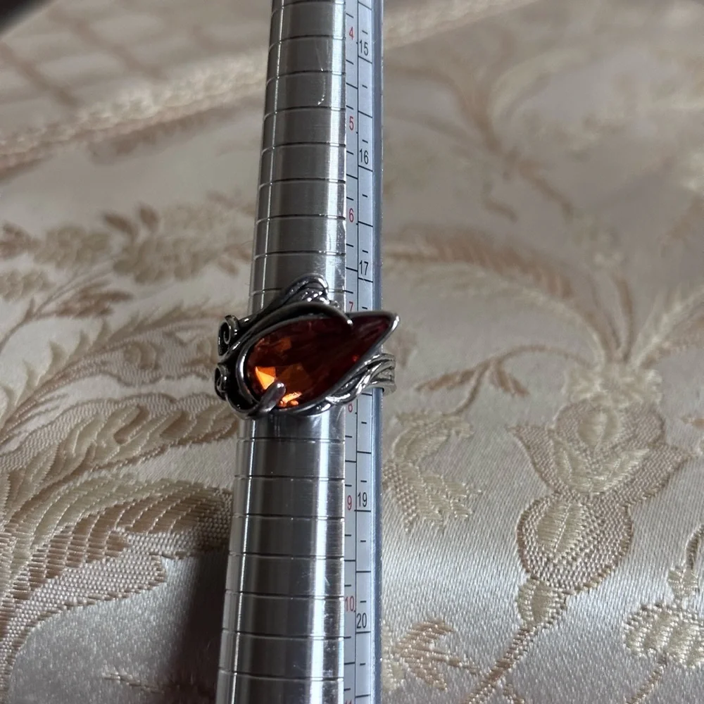 Ring in silver metal intricate with teardrop shaped amber color stone